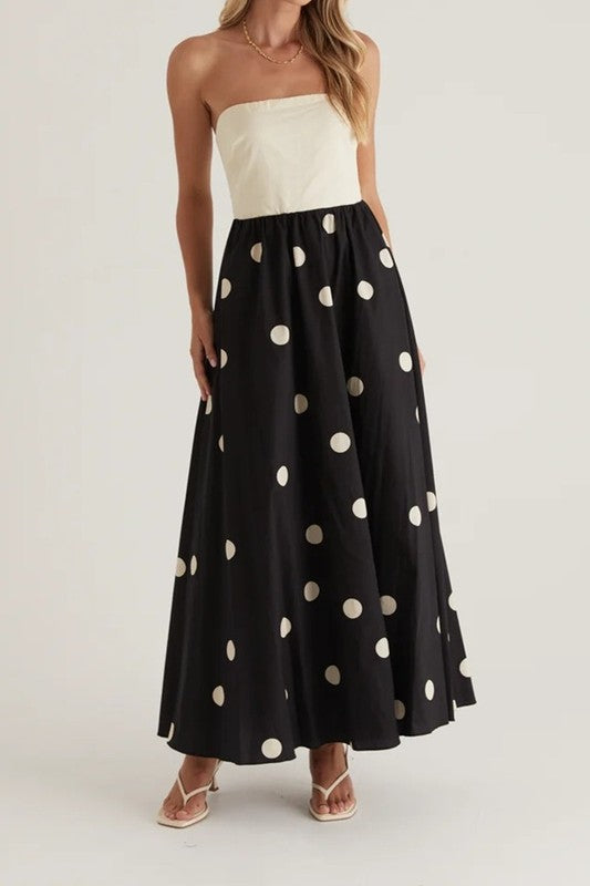Featuring a structured white bodice and a flowing black skirt adorned with cream polka dots, this dress makes a statement with its bold yet classic design.

Ideal for daytime events or summer evenings, it offers effortless charm and sophistication. Style it with delicate sandals and gold accessories for a chic, elevated look.