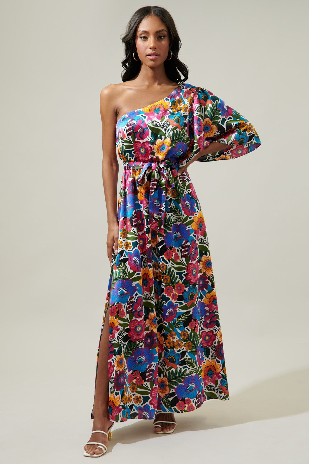 This is a vibrant, satin floral-printed one-shoulder maxi dress. The dress features a bold array of colorful flowers in shades of pink, blue, yellow, and green set against a dark background.

A classic, one shoulder dress with a flowy short sleeve. It maintains a blouson bodice with an elastic waistband that tops a flowy maxi skirt with a side slit. 