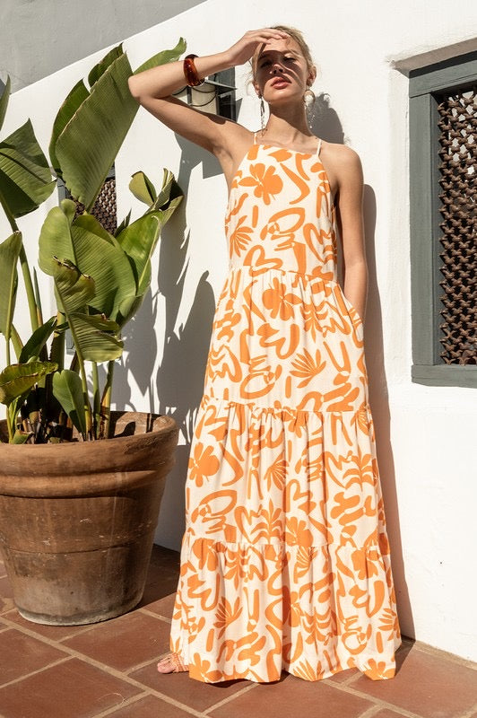 Radiate effortless elegance with the Tangerine Skies Dress, a halter-style dress featuring a bold tropical-inspired orange print on a crisp white base.

Its flows tiered silhouette and relaxed fit make it perfect for sunny days, while the halter neckline and side pockets add both charm and functionality.

Designed with a discreet zipper on the left side for easy wear, this lightweight and breathable dress is made for warm afternoons and sunset strolls.
